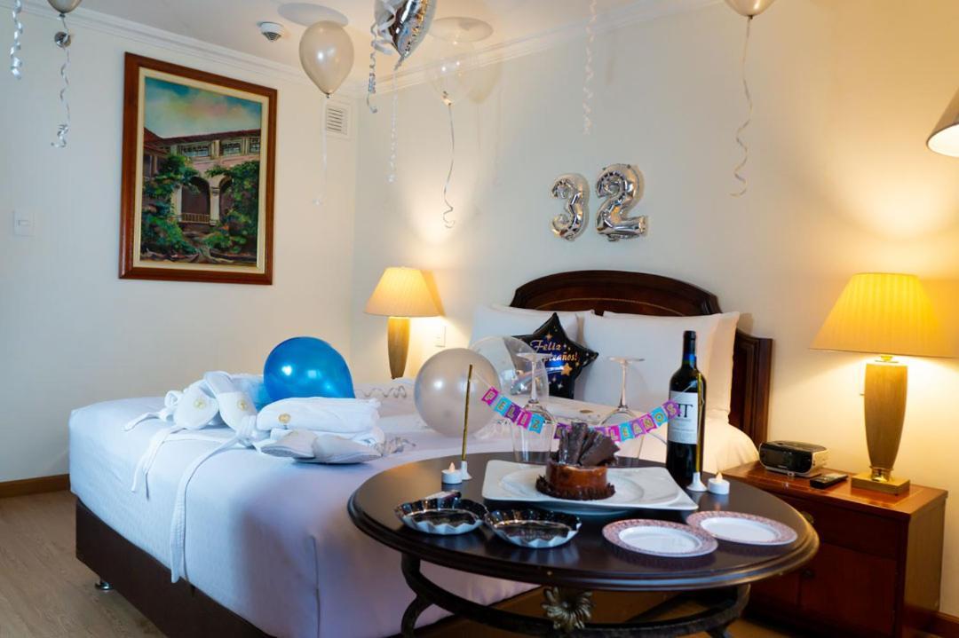 โรงแรมเตเกนดามา โบโกตา ภายนอก รูปภาพ The photo shows a decorated hotel room or a cozy setting for a celebration. In the room, there is a bed with white bedding, two lamps on either side, and a large artwork hanging on the wall. Balloons in various colors, including blue and silver, are 