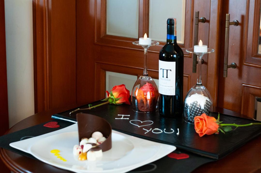 โรงแรมเตเกนดามา โบโกตา ภายนอก รูปภาพ The photo features a romantic setup on a table. There is a plate with a chocolate dessert and some small candies or fruits. Surrounding the dessert are two roses, one orange and one red. In the background, there is a bottle of red wine labeled “IT” a