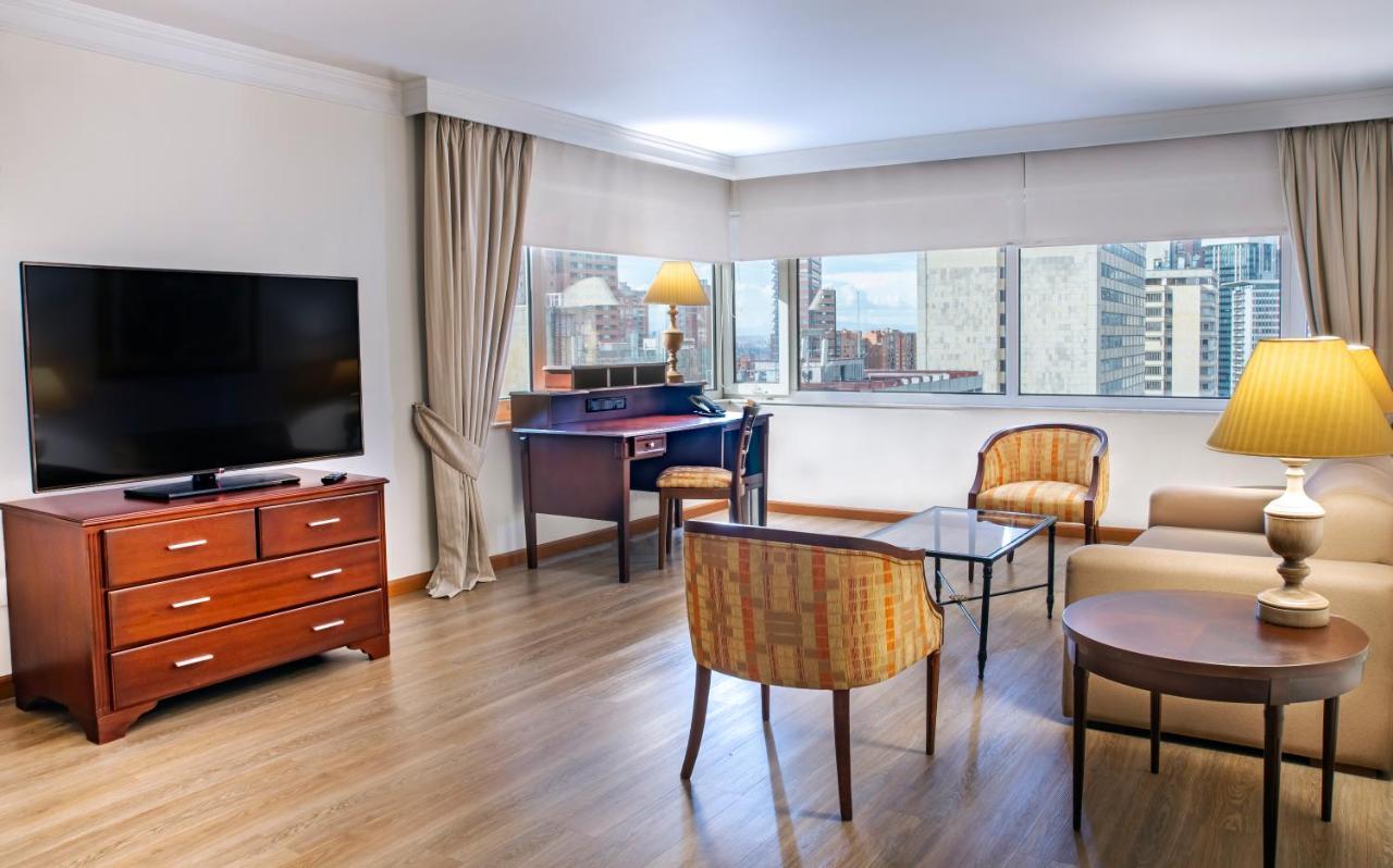 โรงแรมเตเกนดามา โบโกตา ภายนอก รูปภาพ The photo shows a modern living space or hotel room with a cozy, contemporary design. 

- **Furniture**: There is a wooden TV stand with a flat-screen television mounted on the wall, a coffee table in the center, and two upholstered chairs around it.