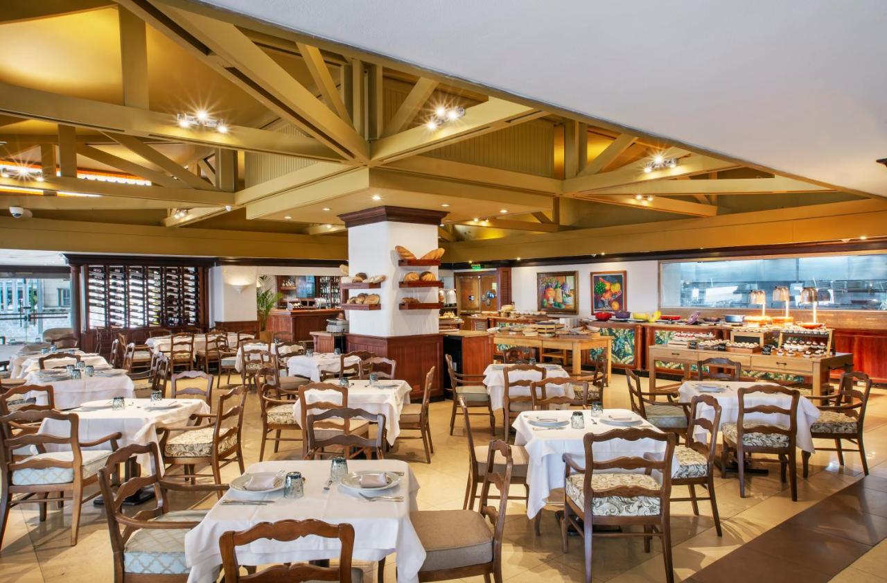 โรงแรมเตเกนดามา โบโกตา ภายนอก รูปภาพ The photo shows a restaurant interior featuring a spacious layout with wooden beams on the ceiling. There are several dining tables set with white tablecloths, and each table has chairs arranged around it. The décor is warm and inviting, with a rusti