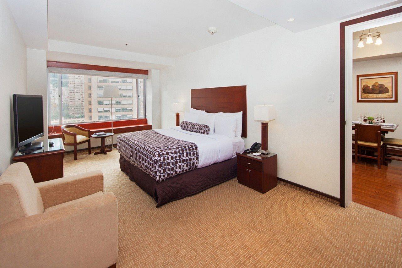 โรงแรมเตเกนดามา โบโกตา ภายนอก รูปภาพ The photo shows a well-furnished hotel room. It features a large bed with a headboard, accompanied by a bedside table and a lamp. There is a seating area with a small couch and a couple of chairs, alongside a window that provides natural light and a 