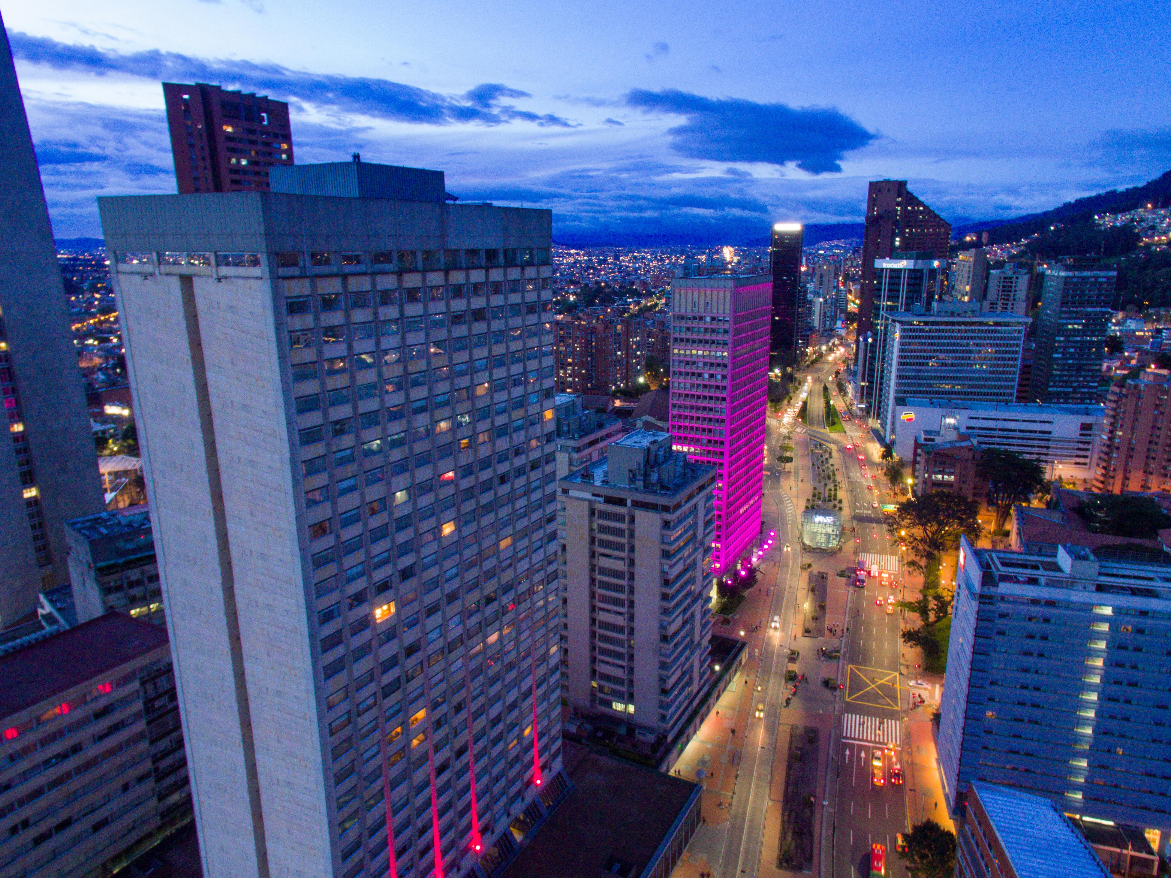 โรงแรมเตเกนดามา โบโกตา ภายนอก รูปภาพ The photo shows an urban landscape during twilight. Skyscrapers and tall buildings are prominently featured, with one building illuminated in pink lights. The street below appears to be busy, with vehicles moving along it. In the background, addition