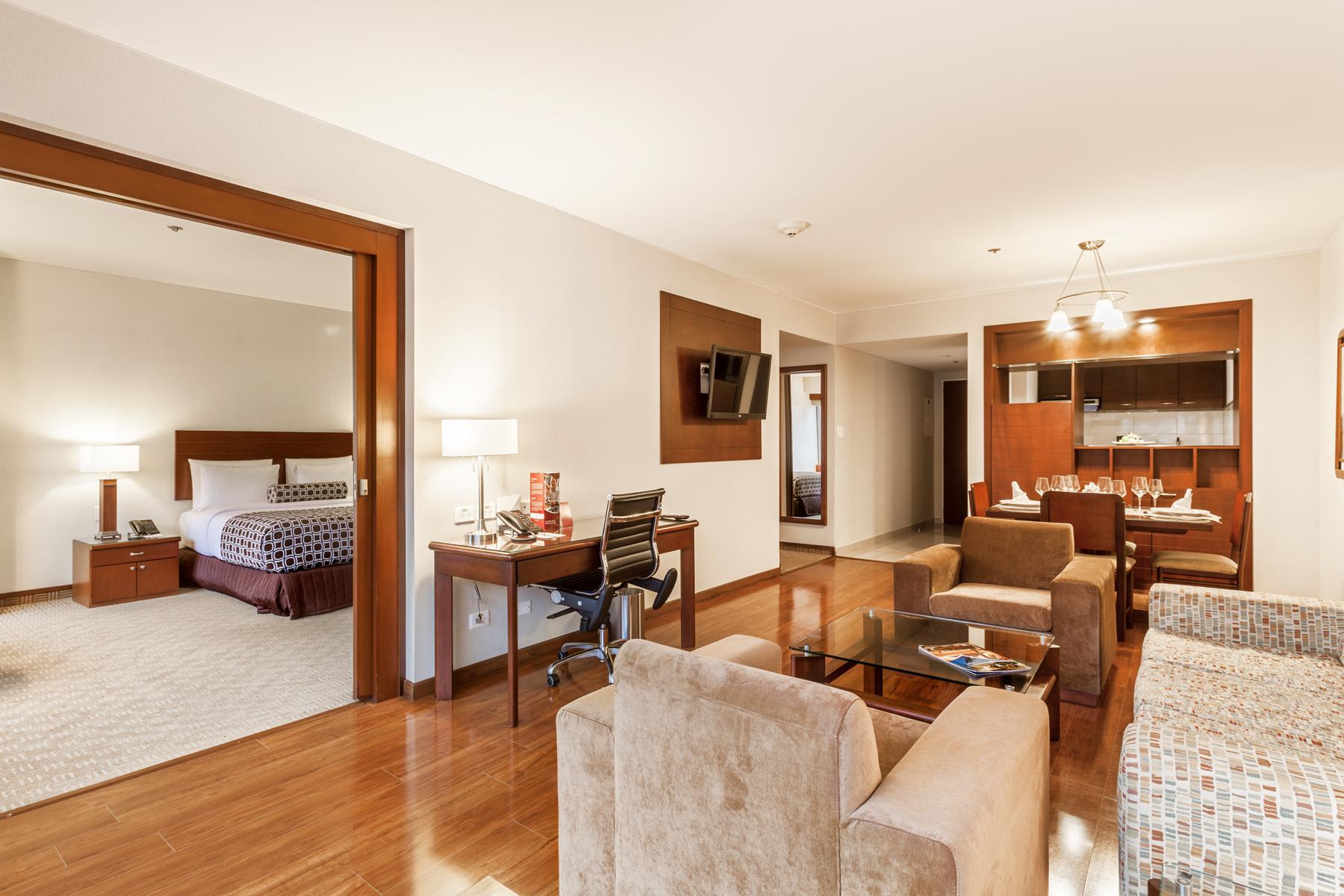 โรงแรมเตเกนดามา โบโกตา ภายนอก รูปภาพ The photo shows a spacious hotel suite. In the foreground, there's a living area with a comfortable seating arrangement, including a beige sofa and a patterned chair. A coffee table sits in the center, and there's a desk with a chair for work. 

In t