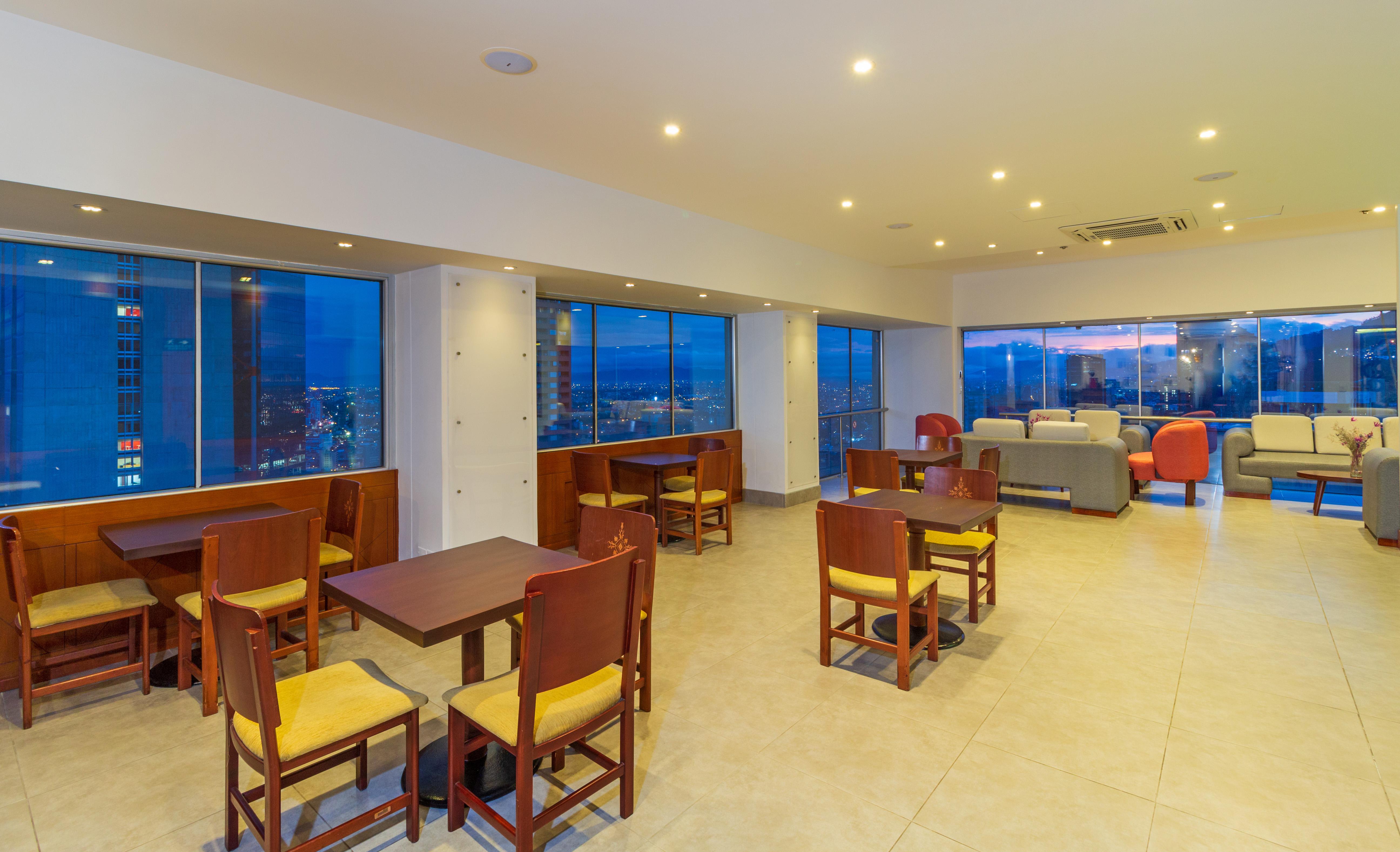 โรงแรมเตเกนดามา โบโกตา ภายนอก รูปภาพ The photo shows a spacious, modern interior of a café or lounge area with large windows, providing a view of the city. The flooring is tiled, and the lighting is warm, creating a welcoming atmosphere. There are several wooden tables with yellow chair