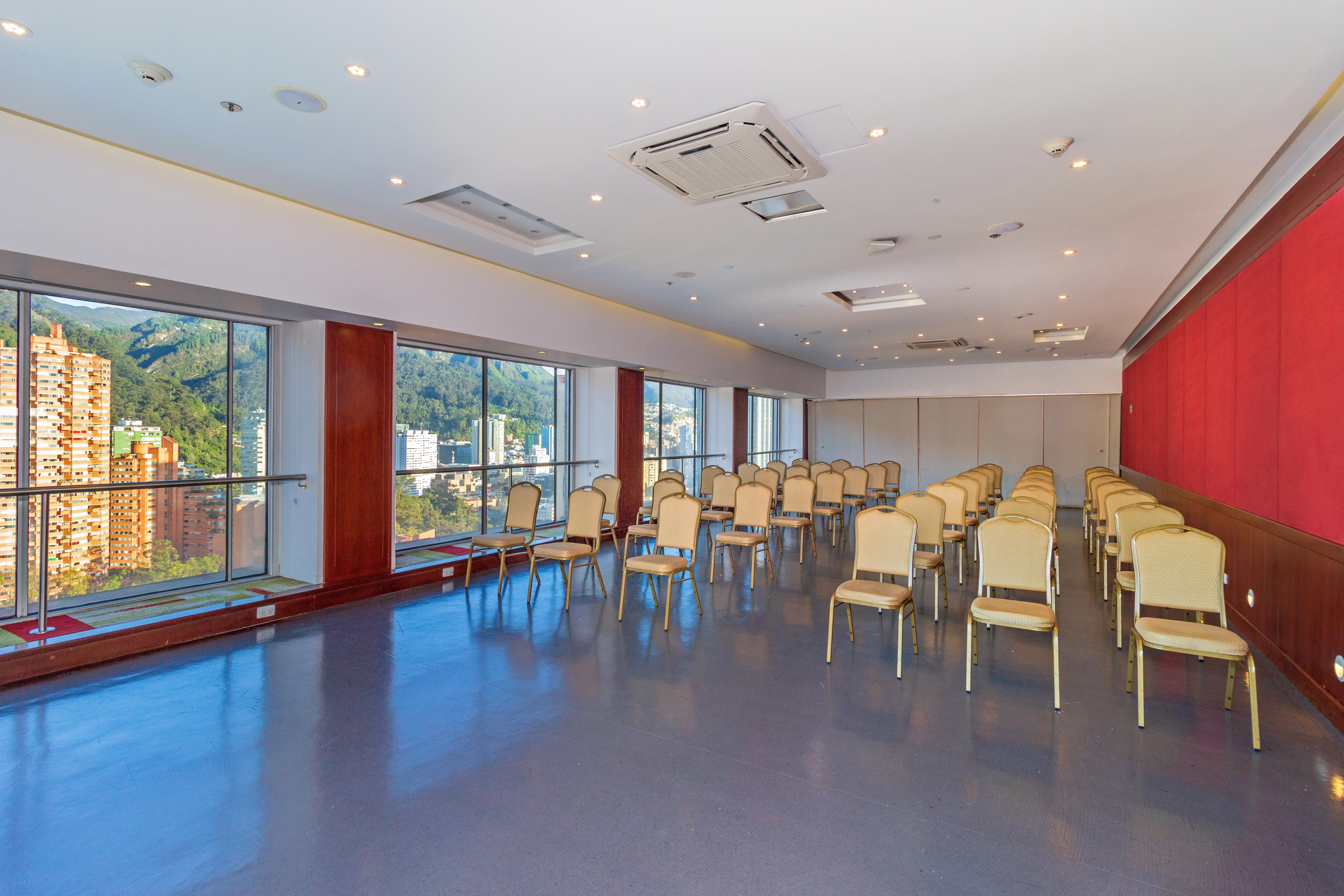 โรงแรมเตเกนดามา โบโกตา ภายนอก รูปภาพ The photo shows a meeting or conference room with a modern design. It features several rows of beige chairs arranged neatly in front of large windows that provide natural light and a view of the outdoors. The walls have a combination of light colors,