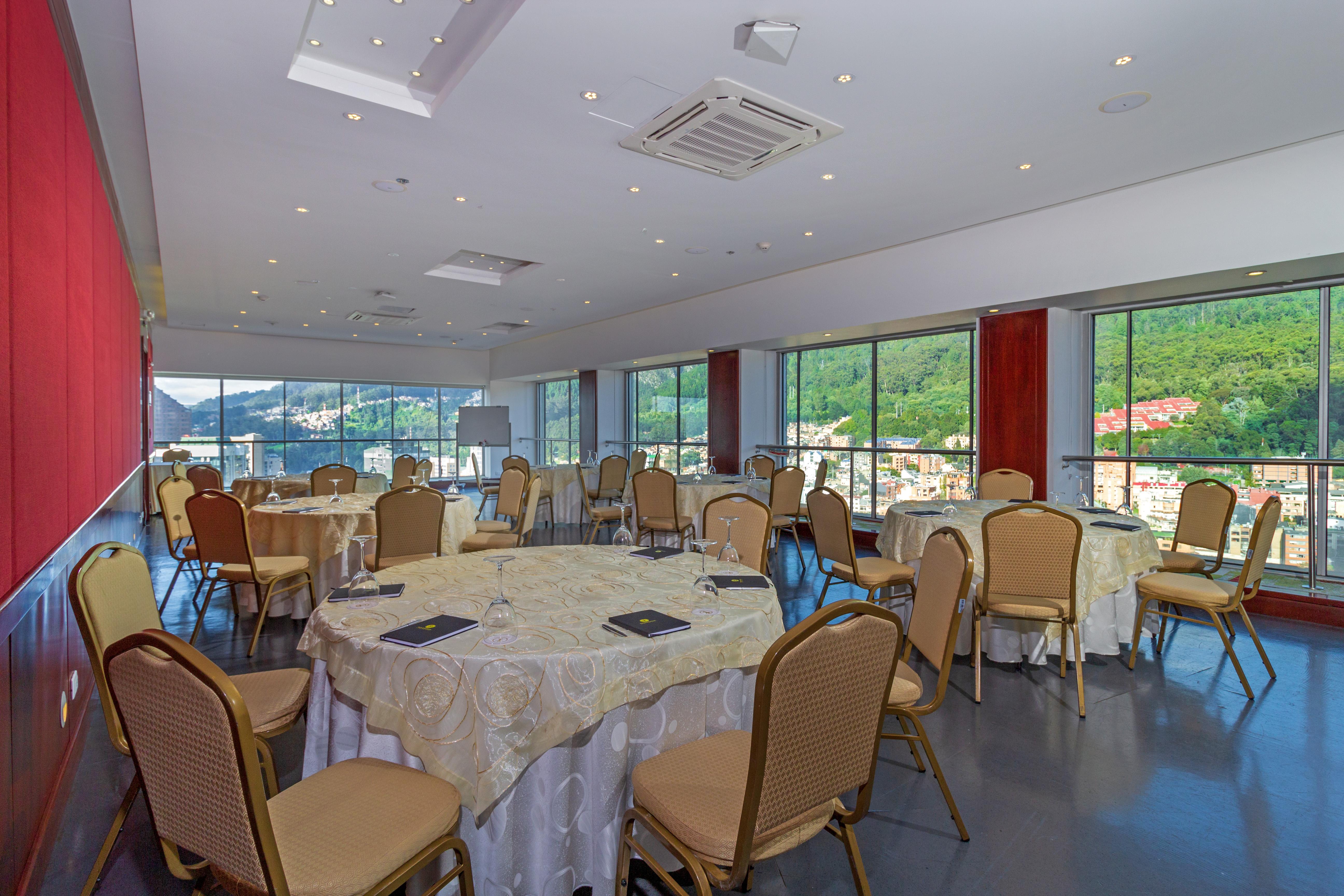 โรงแรมเตเกนดามา โบโกตา ภายนอก รูปภาพ The photo depicts a spacious and elegantly designed meeting room or banquet hall. It features several round tables covered with white tablecloths, each accompanied by beige chairs. The room has large windows that allow natural light to flood in, offe