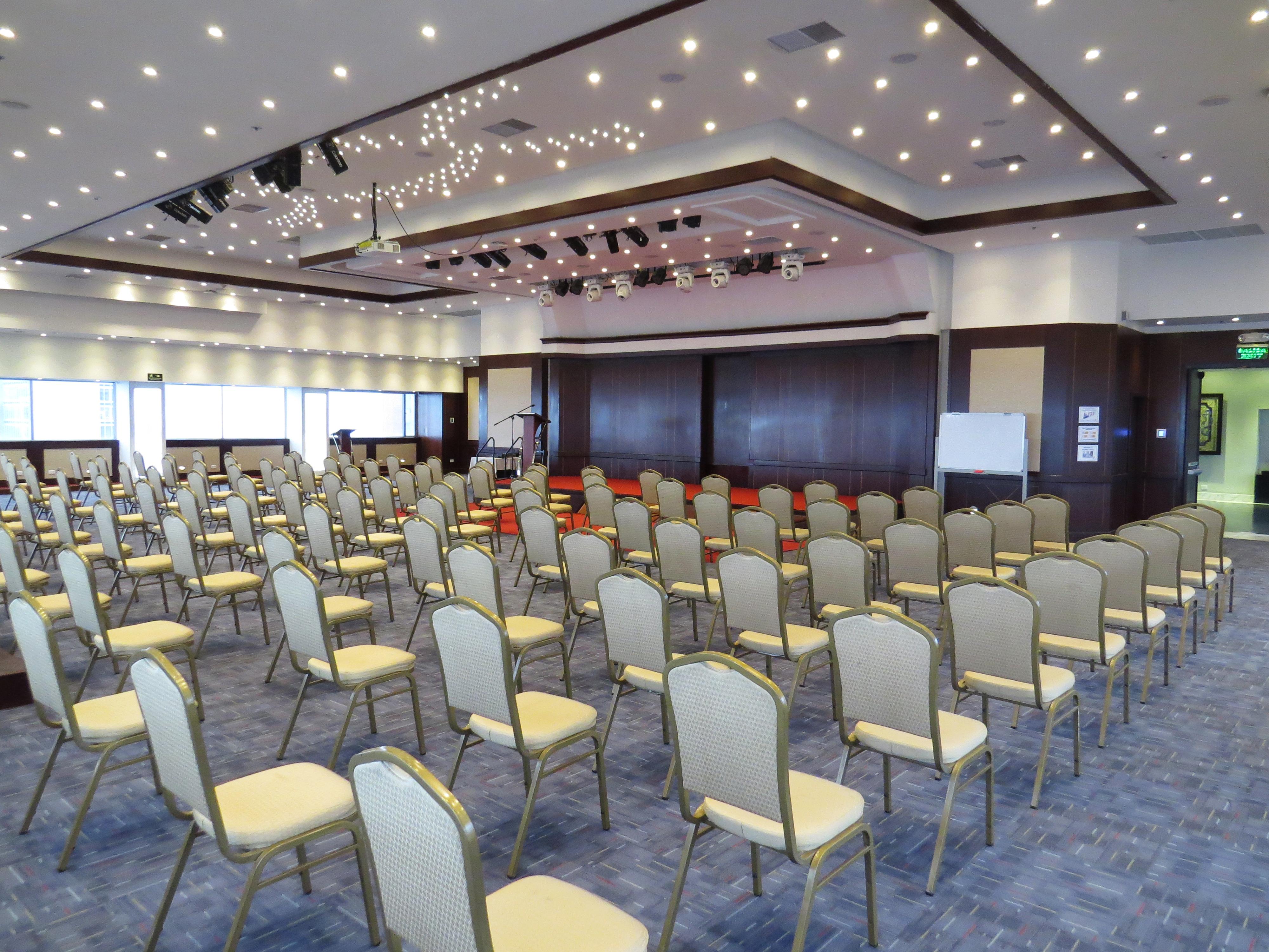 โรงแรมเตเกนดามา โบโกตา ภายนอก รูปภาพ The photo shows a spacious conference or event room set up with numerous empty chairs arranged in rows. The chairs are light-colored with gold accents. The room features a modern design with a high ceiling, decorated with lights that give it a bright