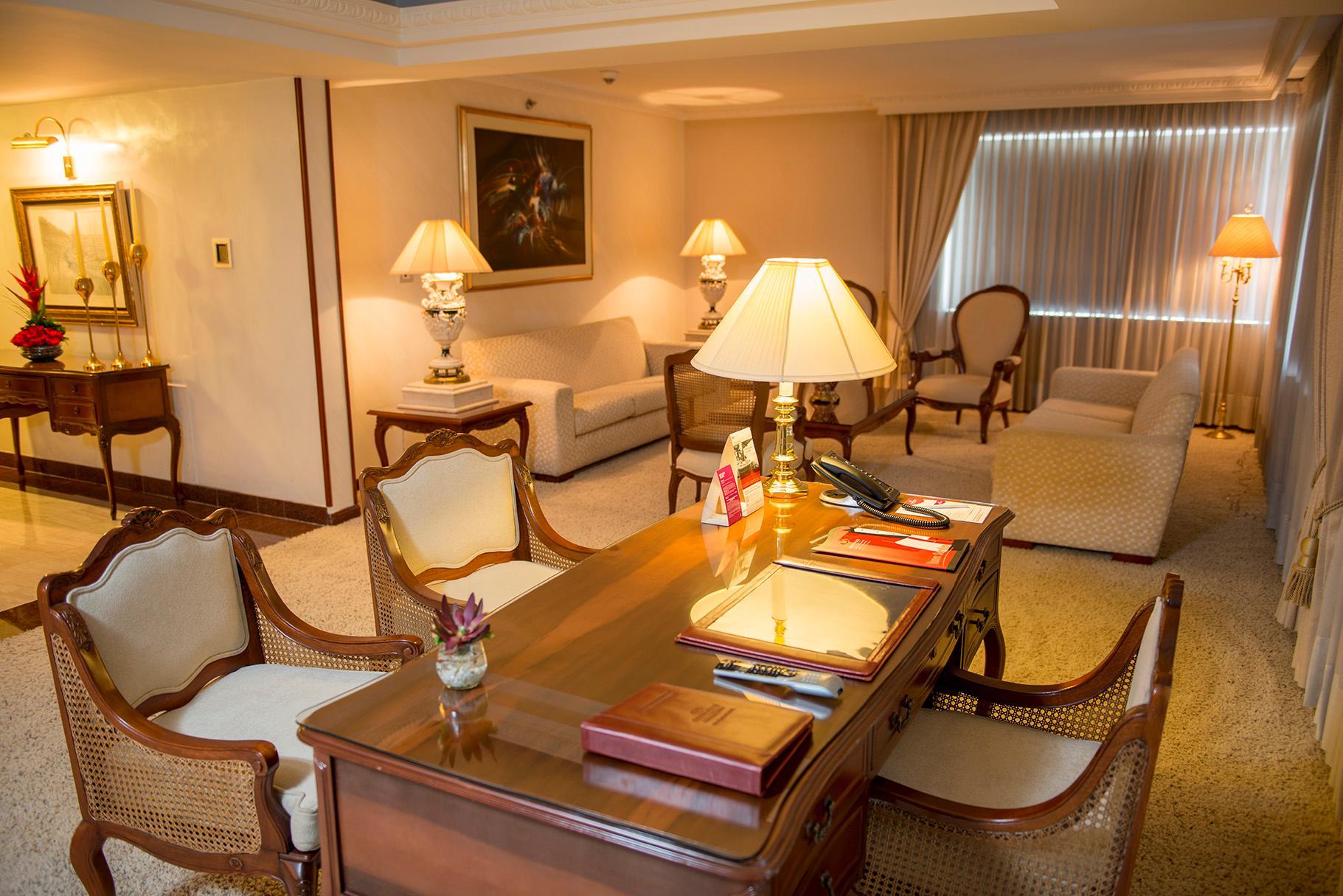 โรงแรมเตเกนดามา โบโกตา ภายนอก รูปภาพ The photo depicts a well-furnished living room or office space. There are elegant pieces of furniture, including a wooden desk with decorative items and stationery on it. Seated around the desk are several upholstered chairs with light-colored fabric