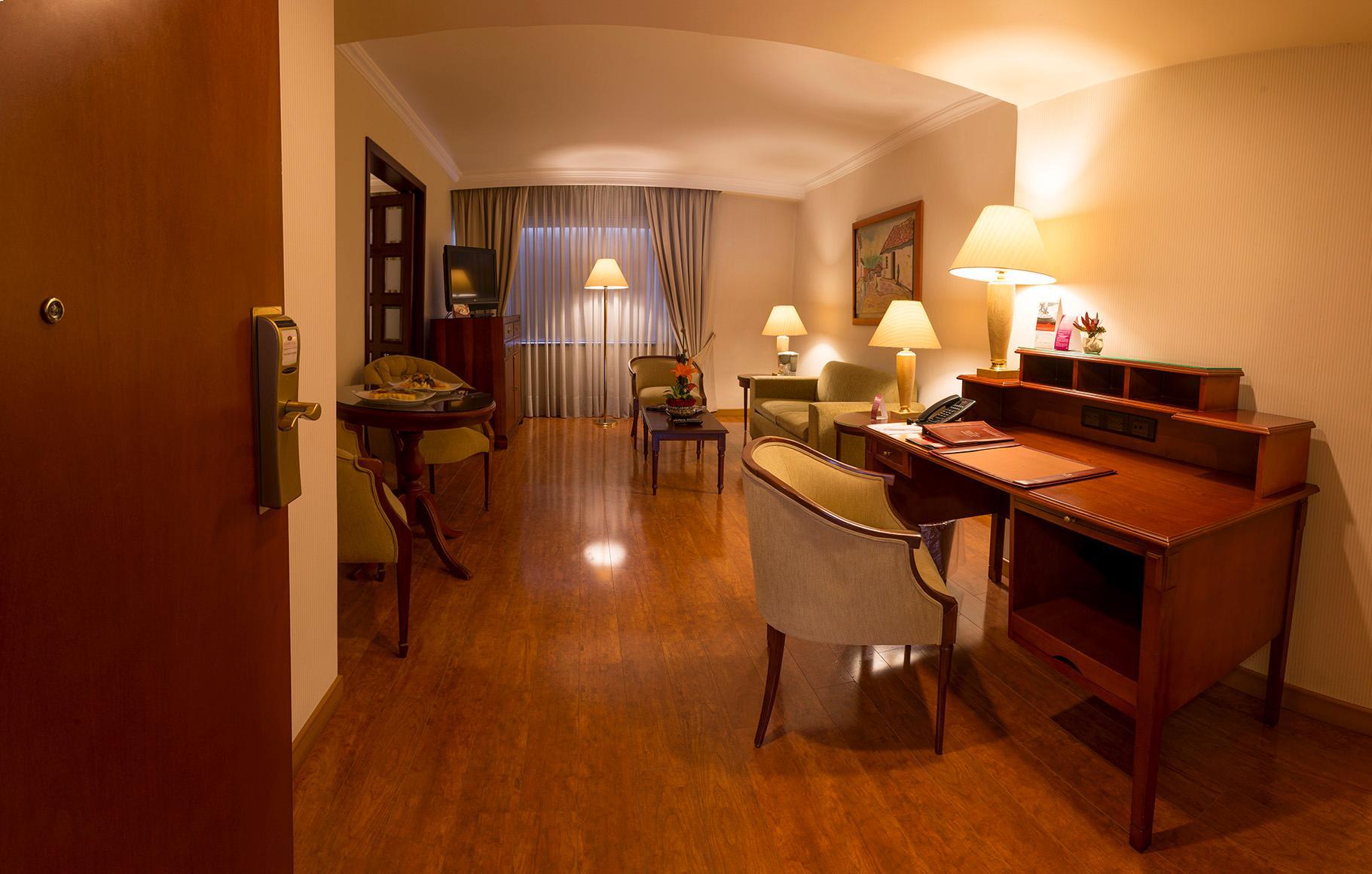 โรงแรมเตเกนดามา โบโกตา ภายนอก รูปภาพ The image shows a well-furnished room that appears to be an office or a living area. It features wooden flooring and soft lighting. On the left, there is a wooden door, and nearby, a small table with a few items on it. To the right, there is a desk w